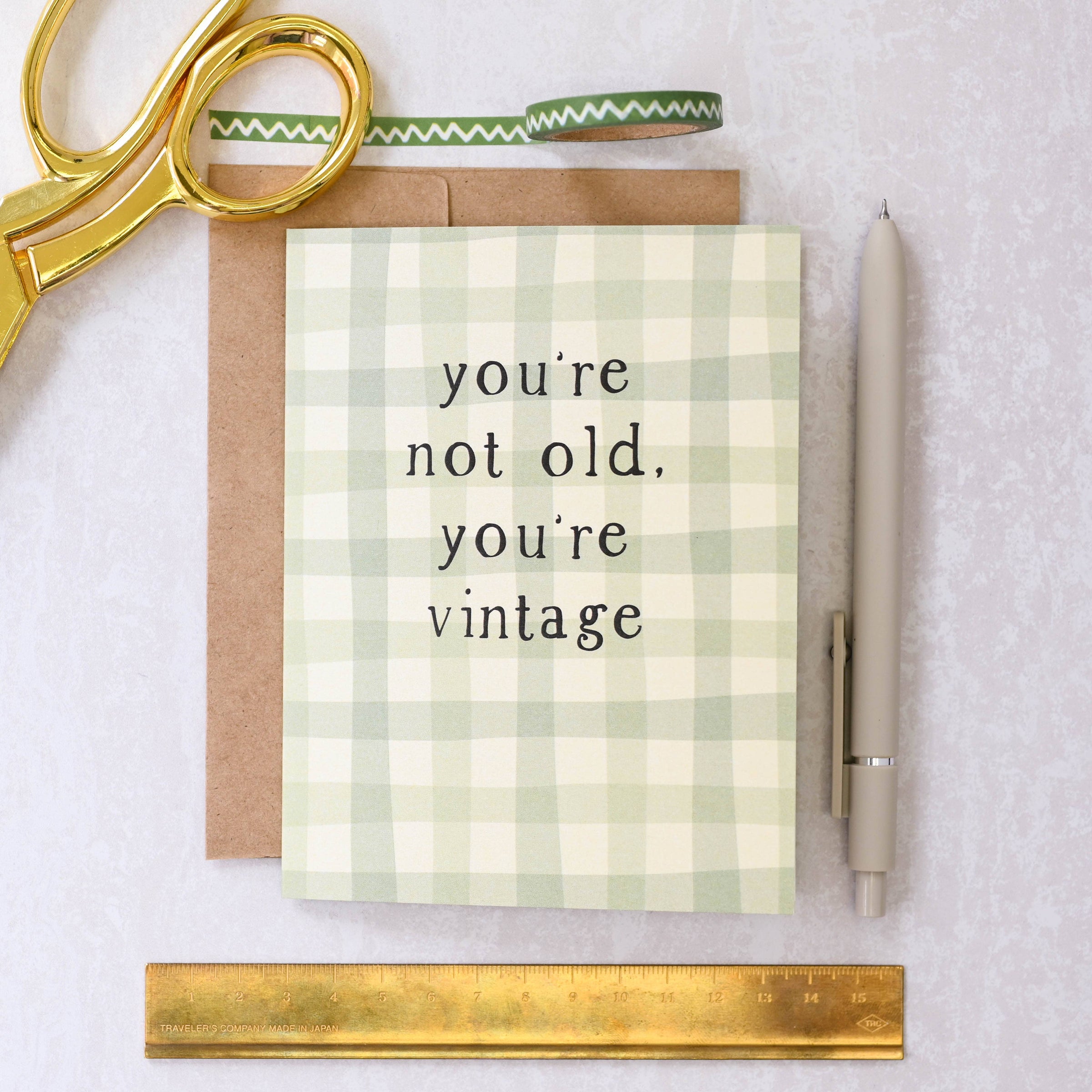 Greeting card with 'you're not old, you're vintage' text on a checkered background, surrounded by stationery items.