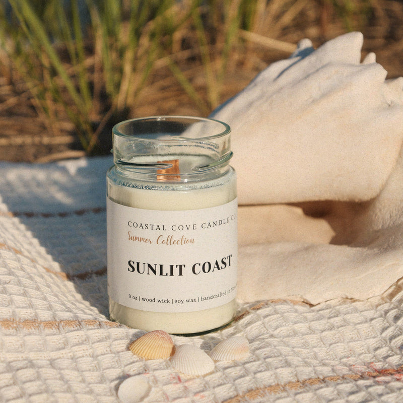 Candle labeled 'Sunlit Coast' on a beach setting with grass and sand in the background