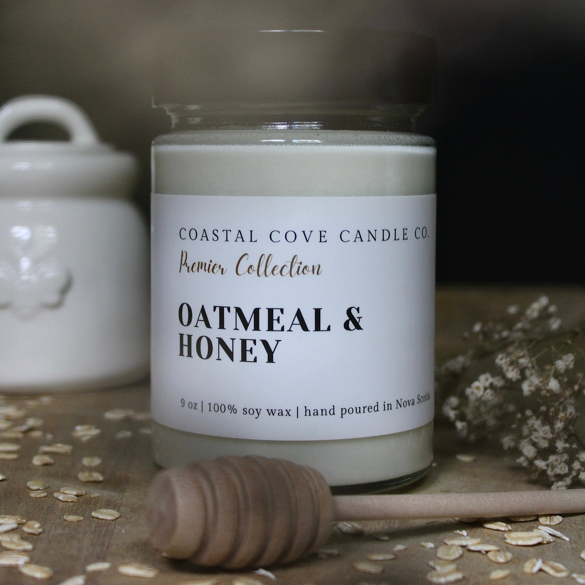 A Coastal Cove Candle Co. 'Premier Collection' candle in a clear glass jar with a white label reading 'Oatmeal & Honey'.