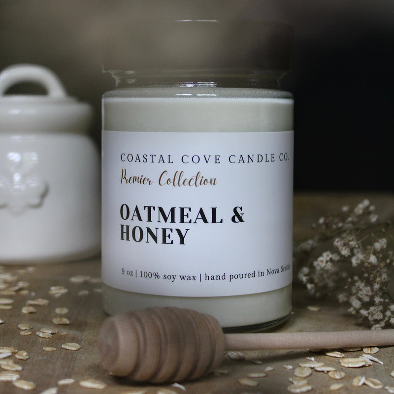 A Coastal Cove Candle Co. 'Premier Collection' candle in a clear glass jar with a white label reading 'Oatmeal & Honey'.