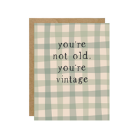 Greeting card with green and beige checkered pattern and text 'you're not old, you're vintage' on a white background.