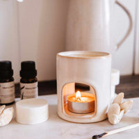 Aromatherapy diffuser with a lit candle on a marble surface, surrounded by essential oils and flowers.
