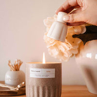 Hand lighting a candle with a decorative label on a wooden surface.