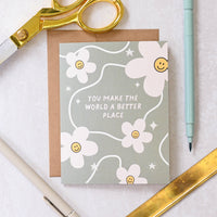 Greeting card with floral design and text on a white surface with stationery items.