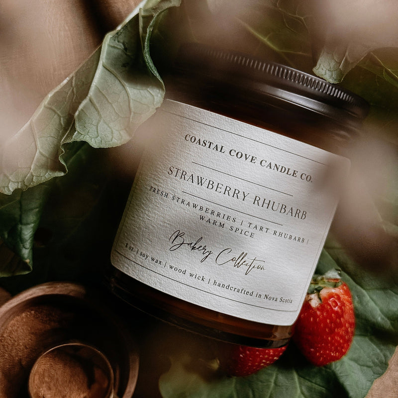 Coastal Cove Candle Co. Strawberry Rhubarb candle with leaves and strawberries on a wooden surface