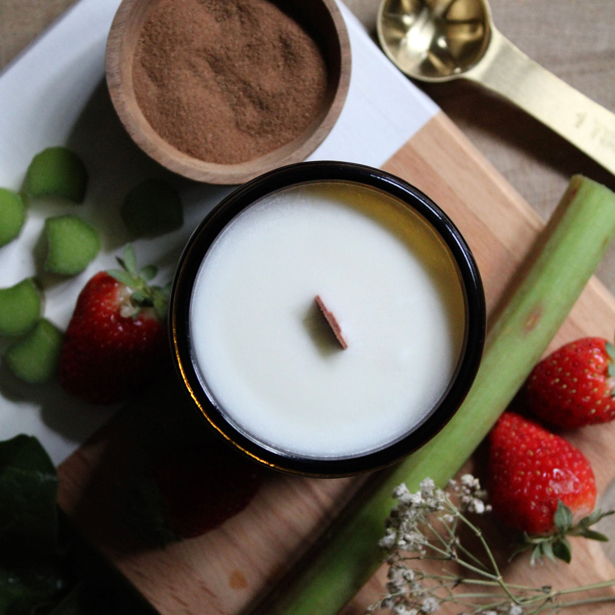 Coastal Cove Candle Co. Strawberry Rhubarb candle with leaves and strawberries on a wooden surface