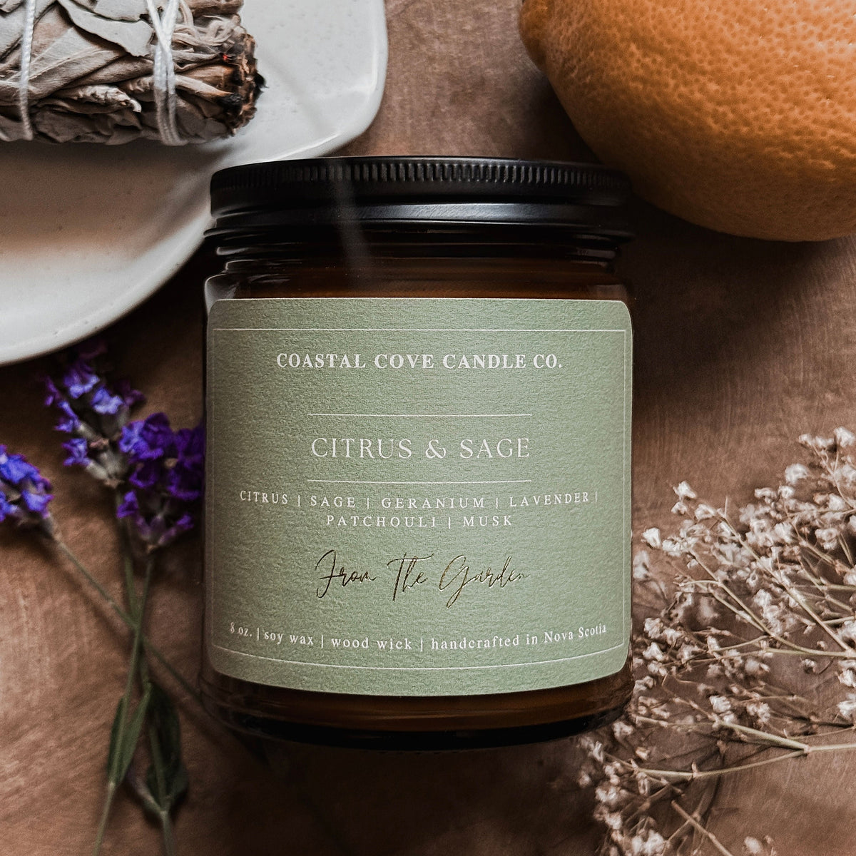 Coastal Cove Candle Co. Citrus & Sage candle with a plate of sage, lemon, and lavender on a wooden surface.