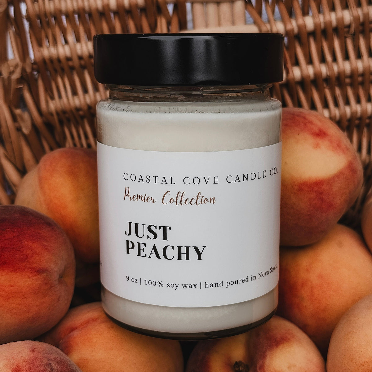 Candle jar labeled 'Just Peachy' surrounded by peaches against a woven basket background
