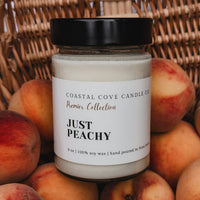 Candle jar labeled 'Just Peachy' surrounded by peaches against a woven basket background
