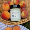 Jar of 'Just Peachy' candle with peaches in a basket on a blanket