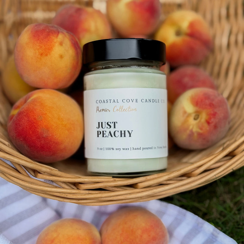 Jar of 'Just Peachy' candle with peaches in a basket on a blanket