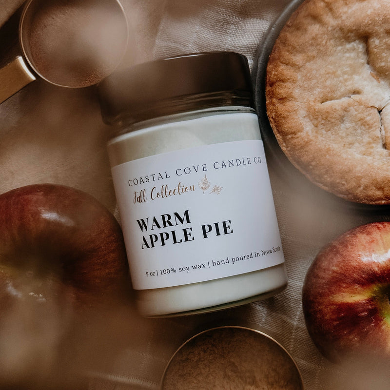 Coastal Cove Candle Co. 'Warm Apple Pie' candle with apples and pie crust on a fabric background
