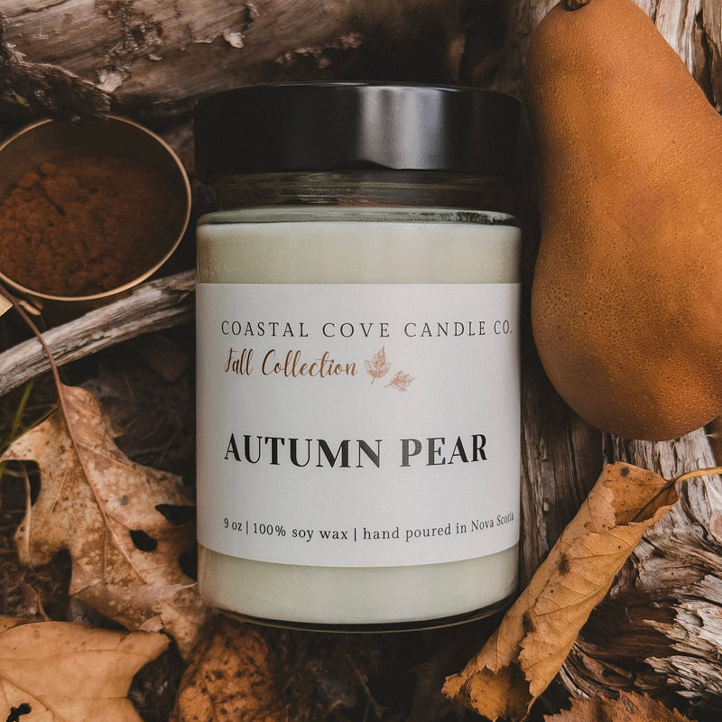 Coastal Cove Candle Co. Autumn Pear candle surrounded by fall elements like leaves and a gourd.