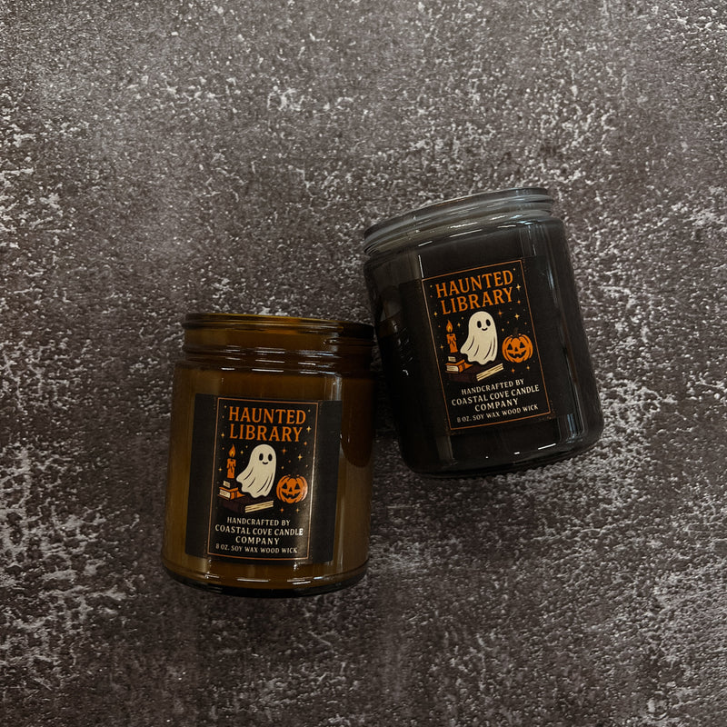 Two 'Haunted Library' candles on a textured gray surface