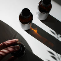 Two brown bottles with black caps on a reflective surface, casting shadows.