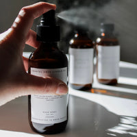 Hand holding a spray bottle with a label, with other similar bottles in the background.