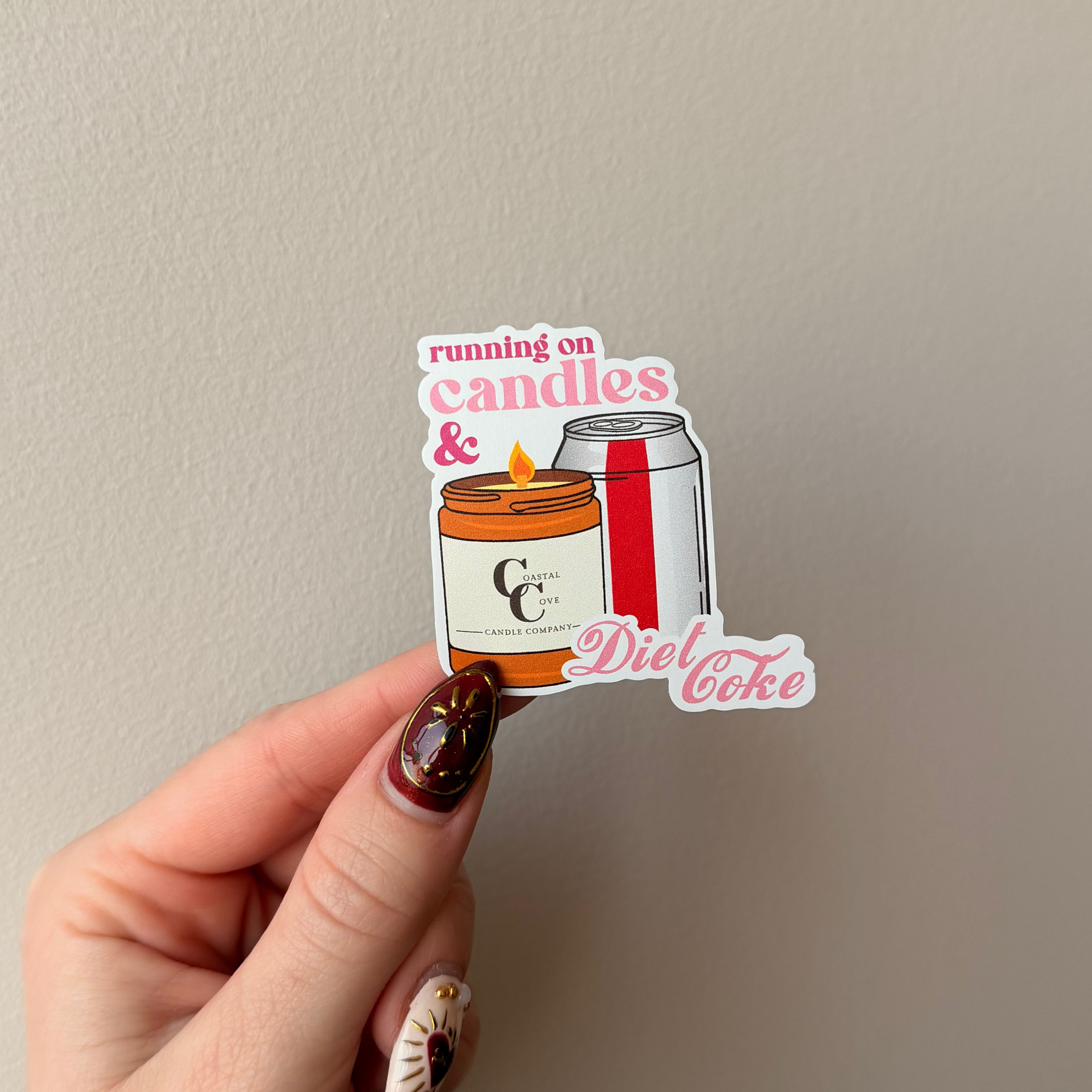 Hand holding a sticker with a design of a can and a candle, against a plain background.