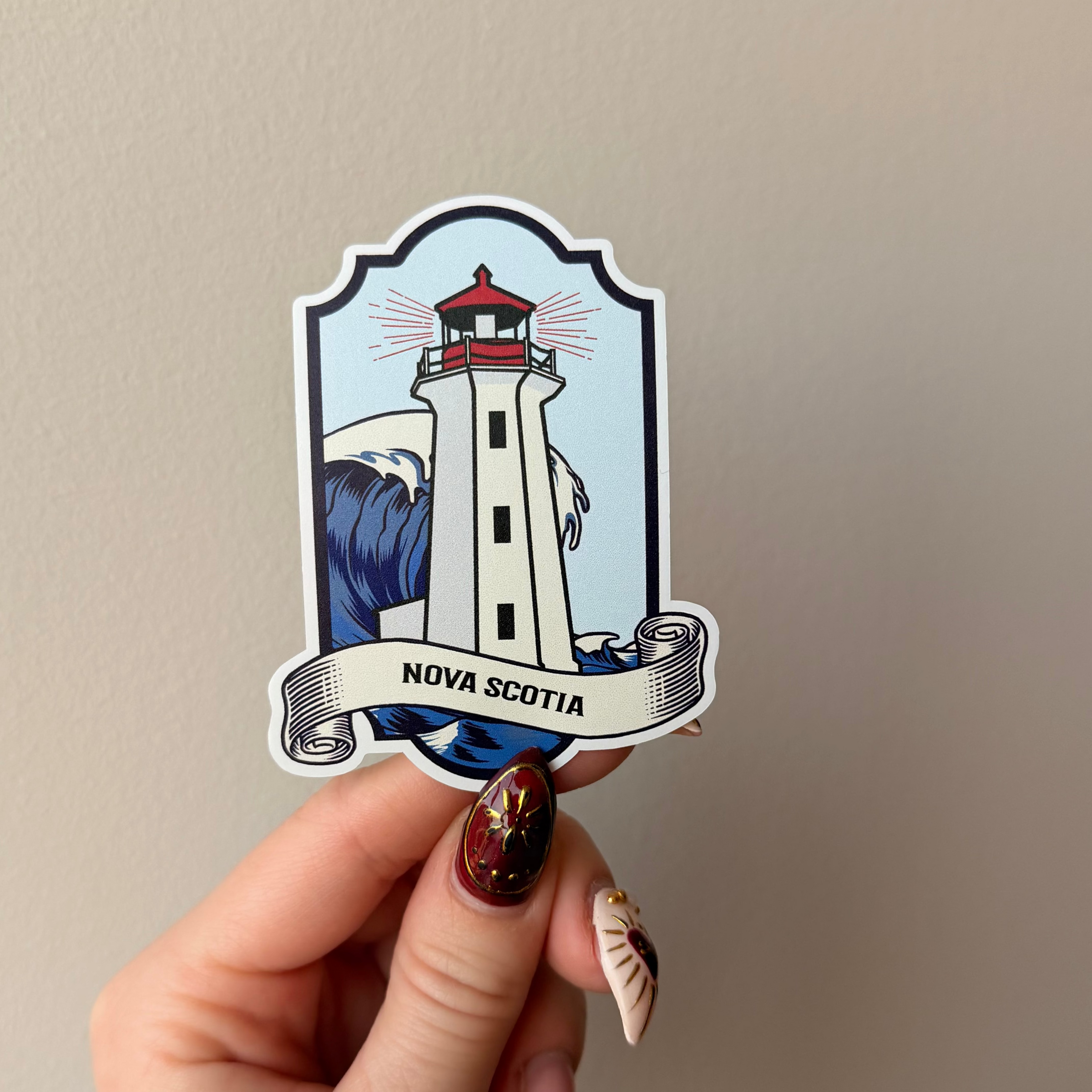 Hand holding a sticker of a lighthouse with 'Nova Scotia' text against a plain background
