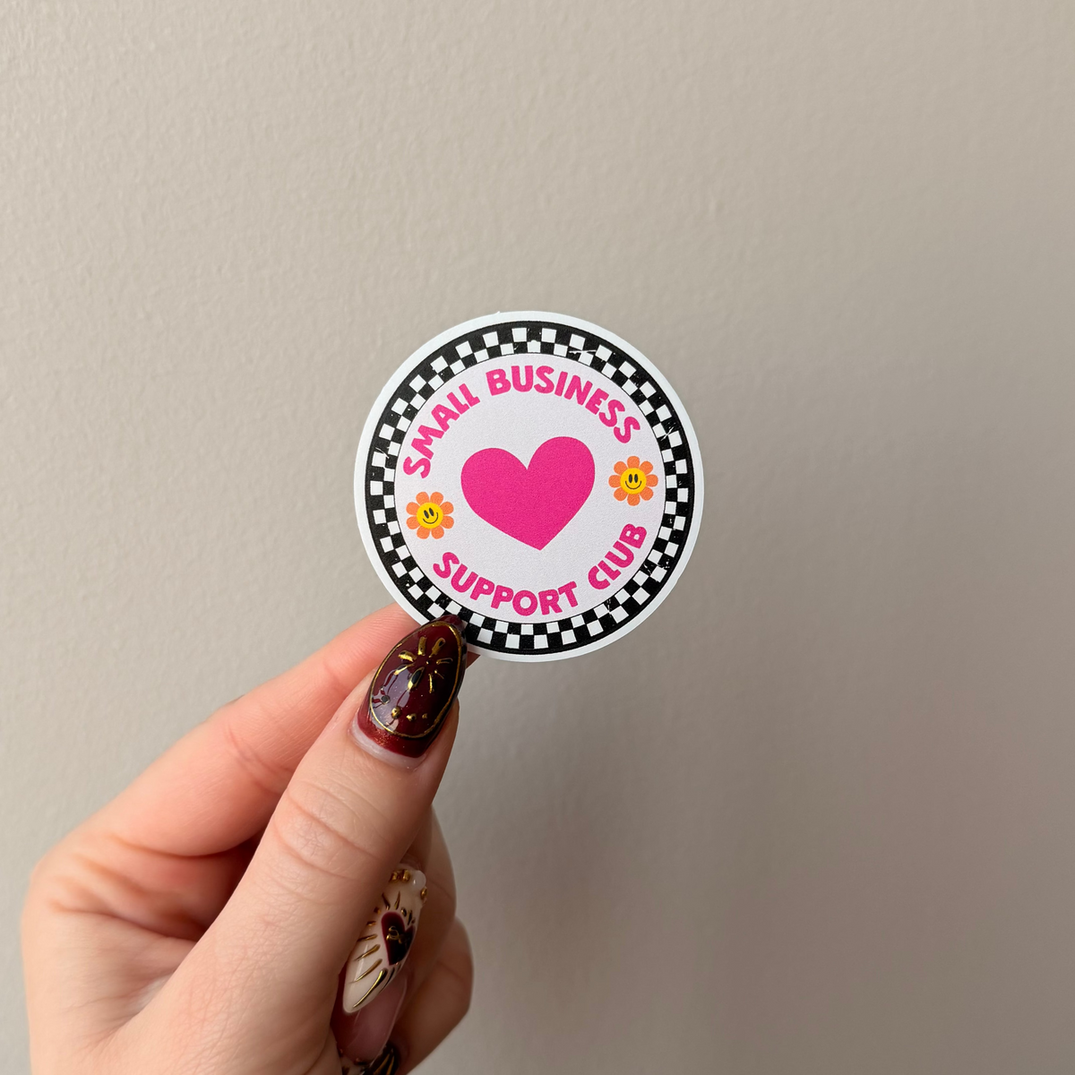 Hand holding a circular sticker with a heart and text on a plain background