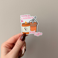 Hand holding a sticker with a coffee cup and candles design against a plain background