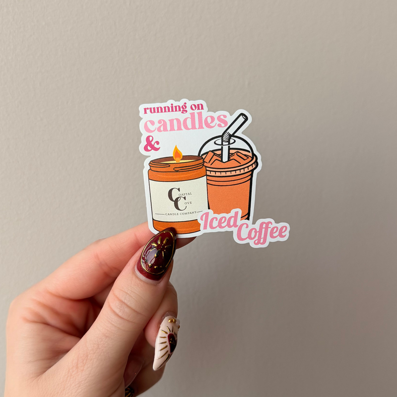 Hand holding a sticker with a coffee cup and candles design against a plain background