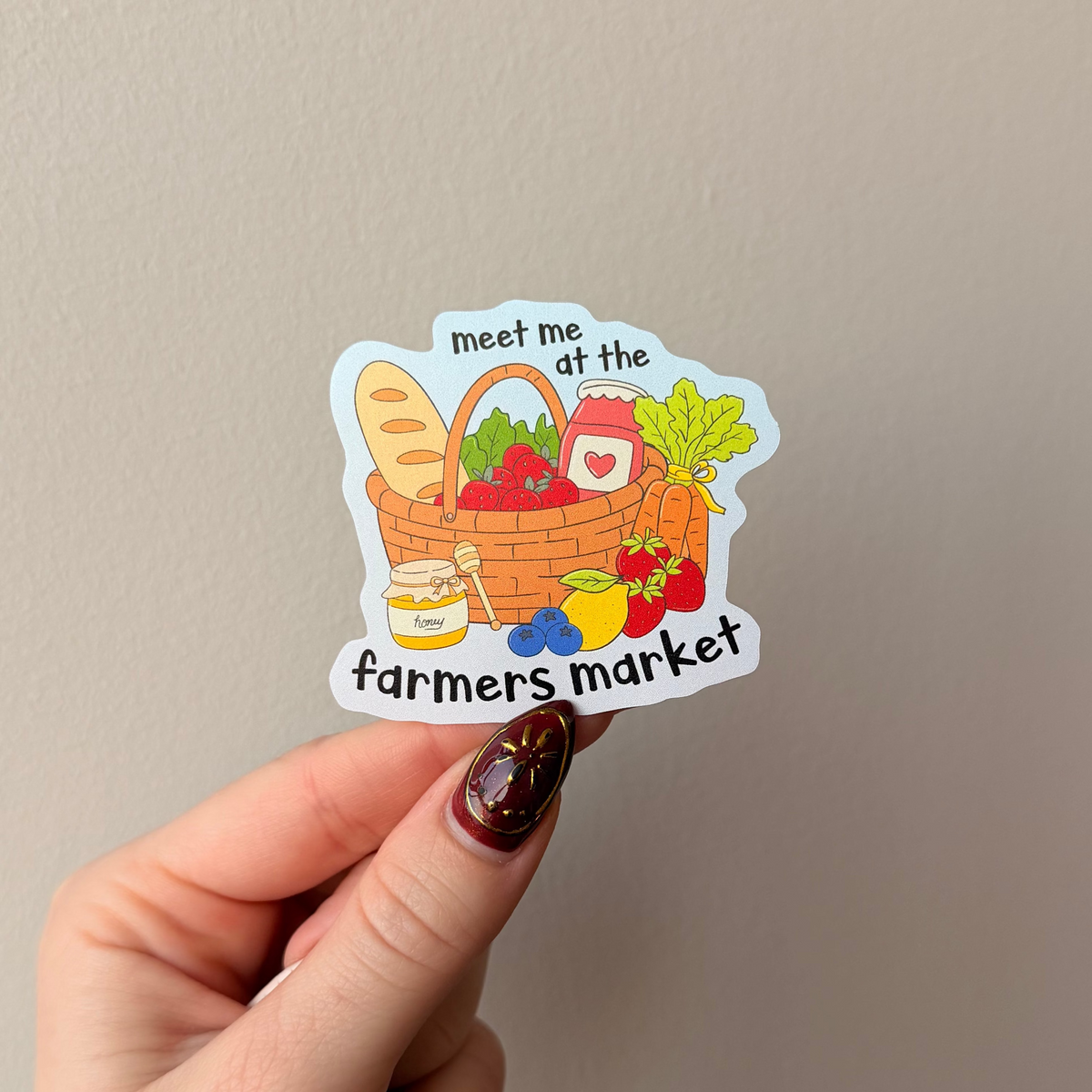 Hand holding a sticker with a farmers market design against a plain background