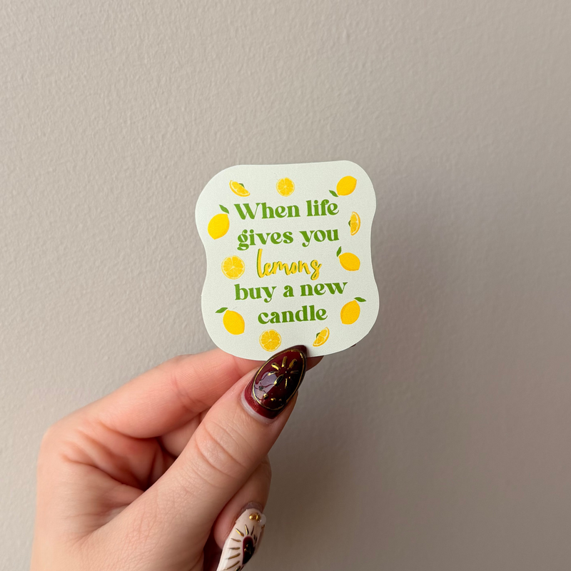 Hand holding a sticker with lemon illustrations and text against a plain background