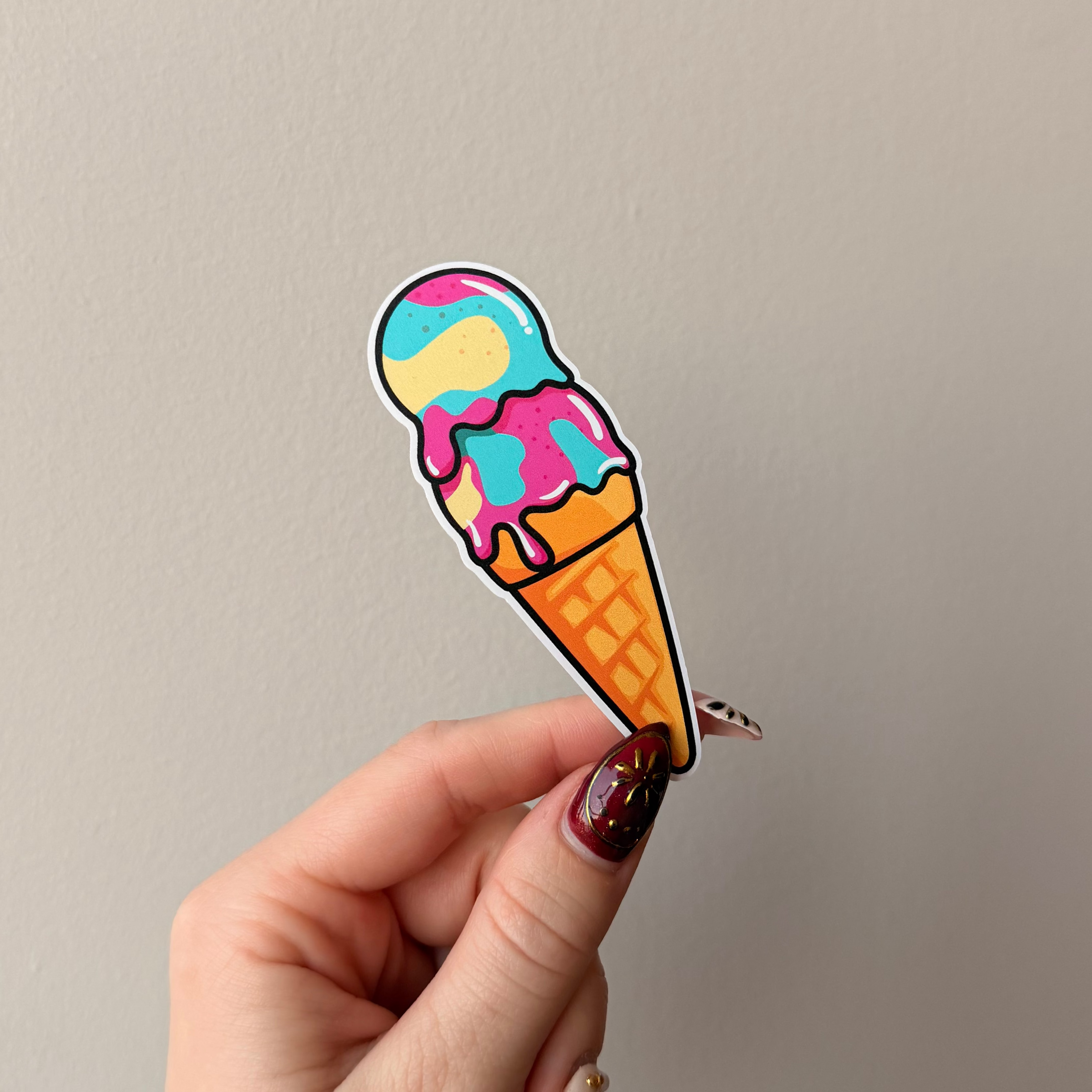 Hand holding a colorful ice cream cone-shaped sticker against a plain background