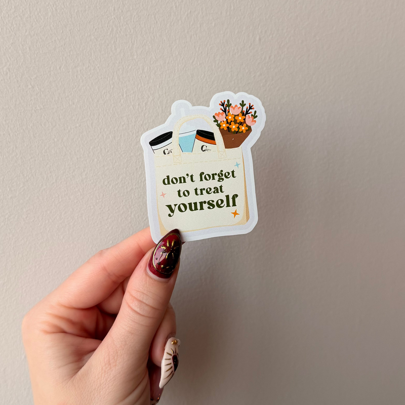 Hand holding a sticker with 'don't forget to treat yourself' text against a plain background