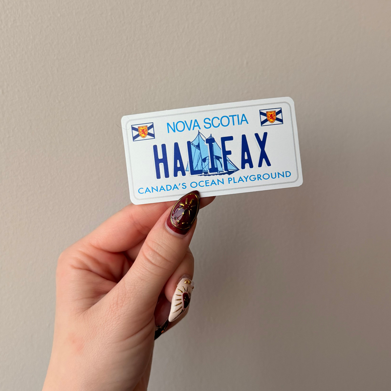 Hand holding a Halifax, Nova Scotia license plate sticker against a plain background