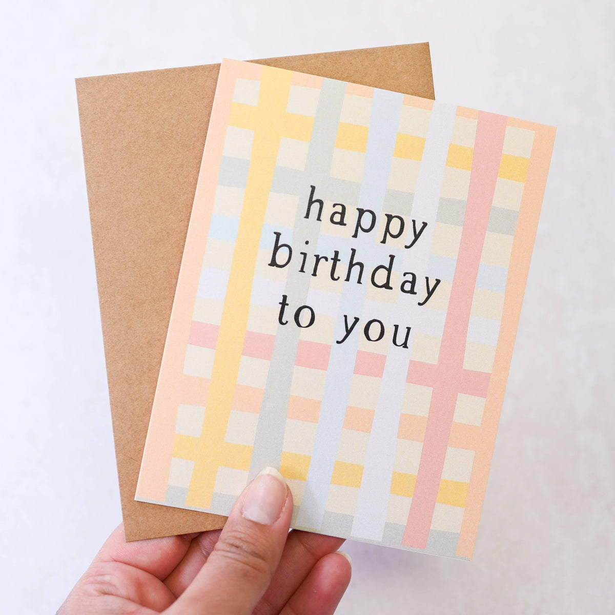Hand holding a birthday card with a checkered pattern and 'happy birthday to you' text.