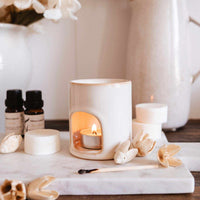 Aromatherapy setup with candles, essential oils, and flowers on a marble surface.