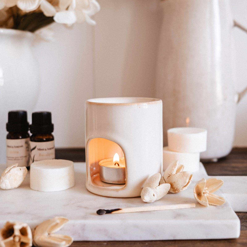 Aromatherapy setup with candles, essential oils, and flowers on a marble surface.